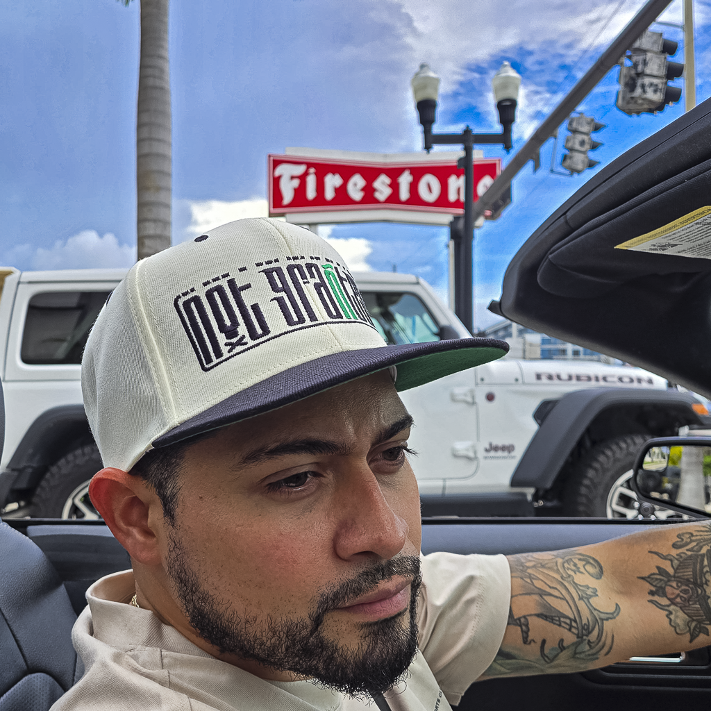 Man wearing a cap with text, sitting in a vehicle with a Firestone sign in the background.