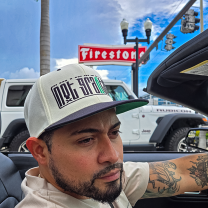 Man wearing a cap with text, sitting in a vehicle with a Firestone sign in the background.