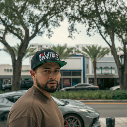 Man wearing a cap with text standing outdoors with cars and buildings in the background